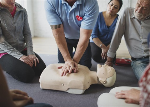 A First Aid Training facilitator demonstrates CPR on a mannequin while people in the class watch